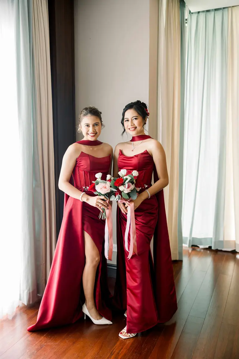 Two guests in deep red gowns with a bouquet