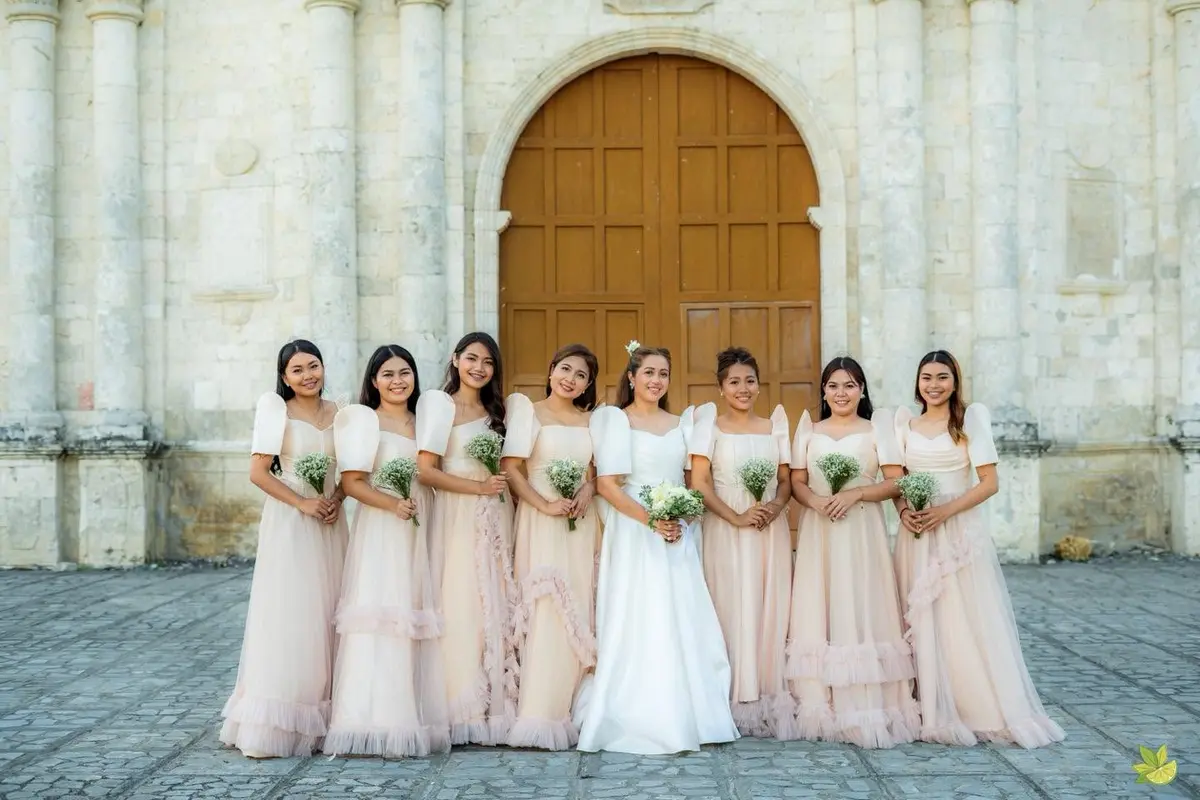 Bridal party in blush gowns outside a stone church